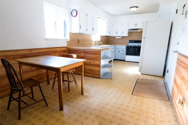 kitchen with wood walls, light countertops, wainscoting, freestanding refrigerator, and electric range