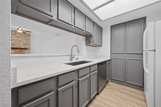 kitchen featuring gray cabinetry, a sink, stainless steel dishwasher, freestanding refrigerator, and light countertops