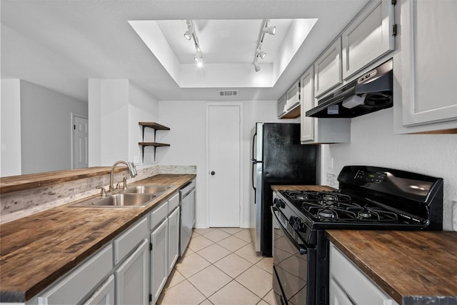 kitchen featuring black gas range, under cabinet range hood, butcher block counters, and a sink