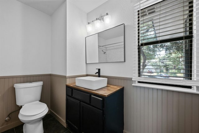 full bathroom featuring tile patterned floors, vanity, toilet, and wainscoting