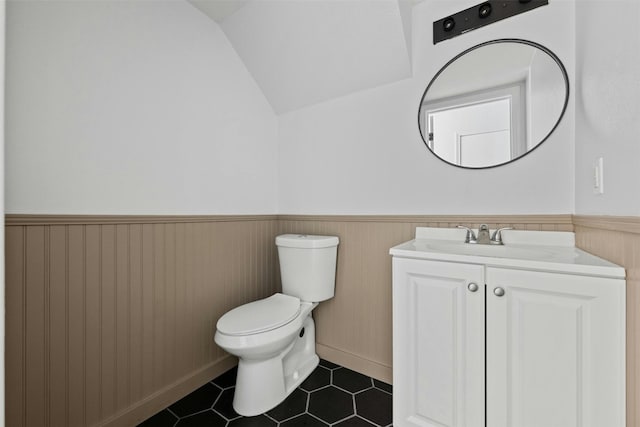 bathroom with tile patterned floors, a wainscoted wall, toilet, lofted ceiling, and vanity