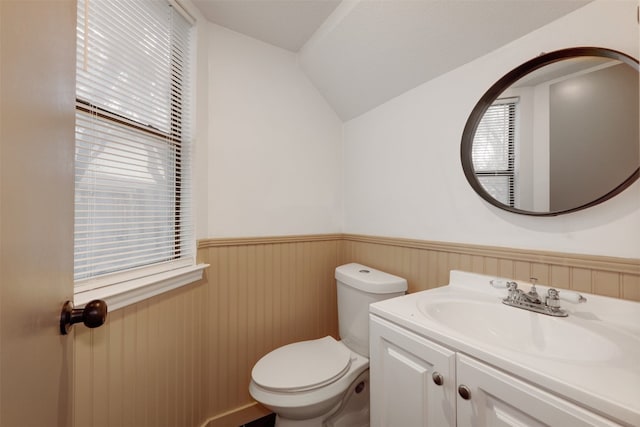 half bathroom featuring wainscoting, toilet, vanity, and vaulted ceiling