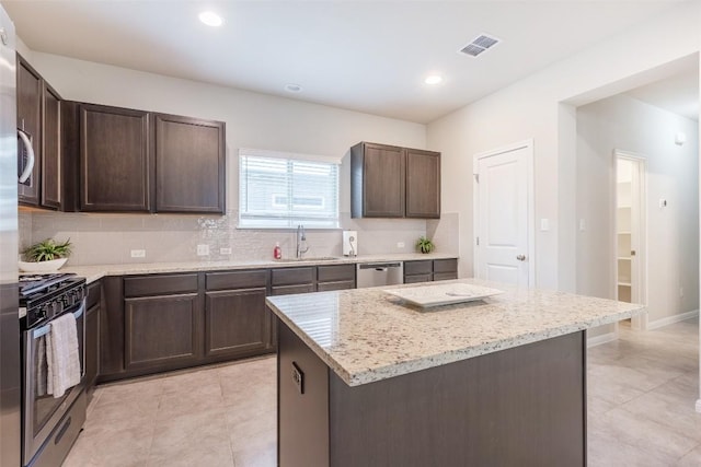 kitchen featuring a sink, backsplash, stainless steel appliances, dark brown cabinetry, and light stone countertops