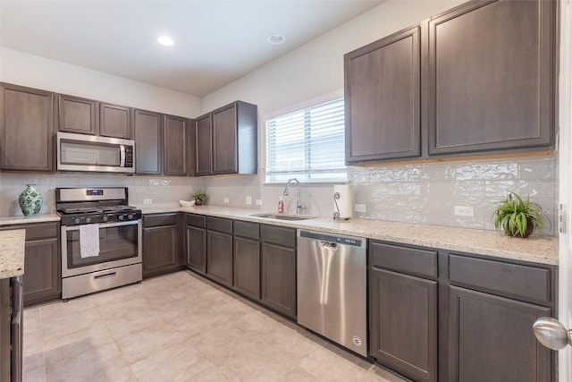 kitchen with a sink, decorative backsplash, light stone counters, and stainless steel appliances