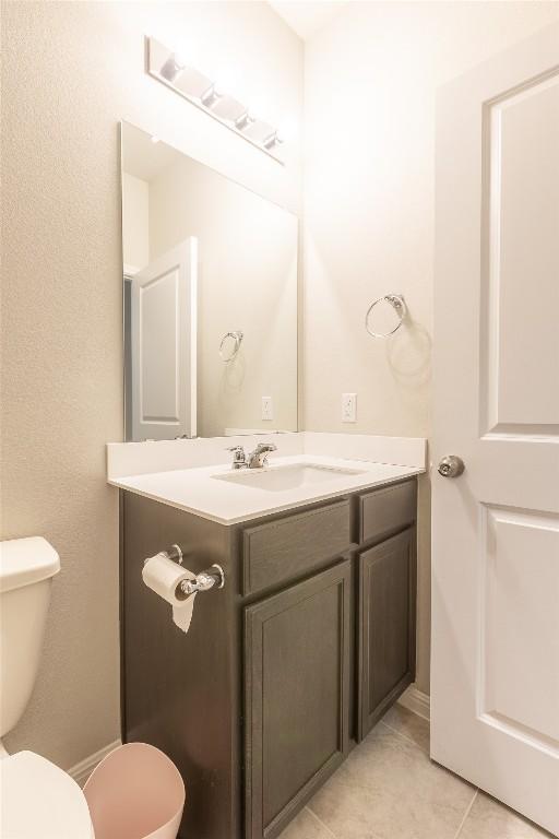 half bathroom featuring tile patterned flooring, toilet, and vanity