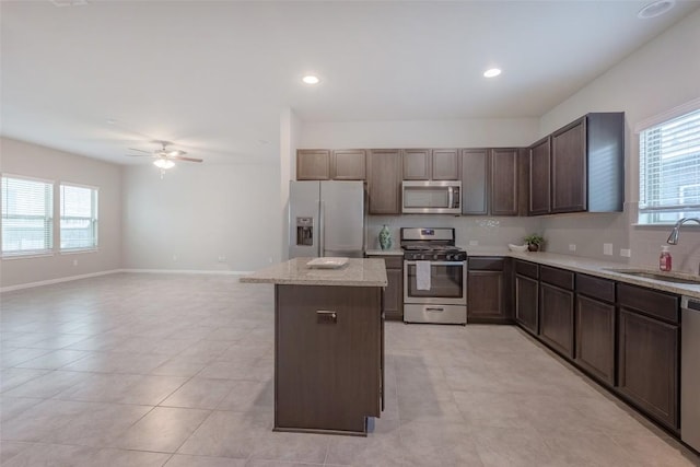 kitchen with light stone countertops, a ceiling fan, a kitchen island, a sink, and appliances with stainless steel finishes