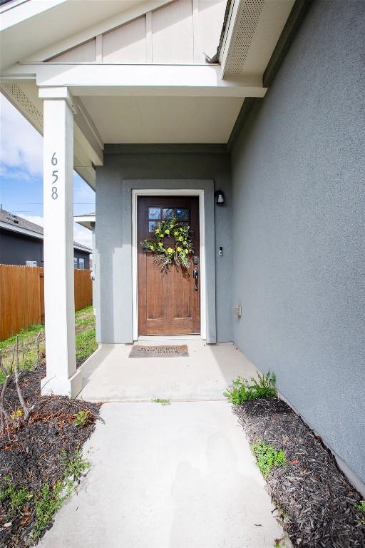 entrance to property featuring stucco siding and fence