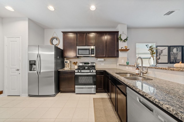 kitchen with dark brown cabinetry, stone counters, decorative backsplash, stainless steel appliances, and a sink