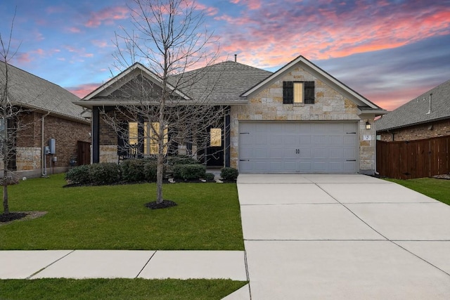 view of front of home with stone siding, a lawn, driveway, and a garage