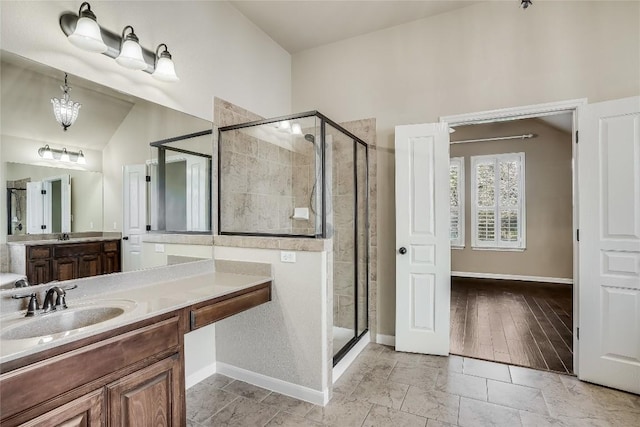 full bath with baseboards, vanity, a shower stall, and vaulted ceiling