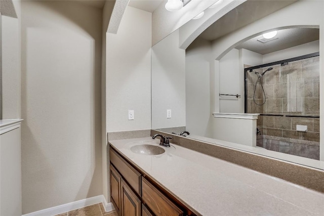 full bath featuring vanity, baseboards, and tiled shower