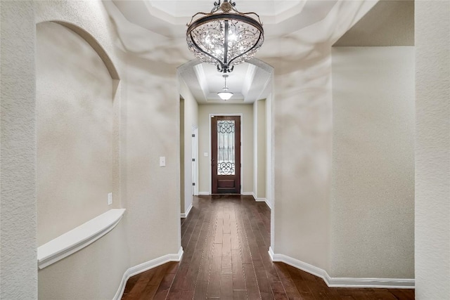 doorway featuring baseboards, dark wood finished floors, arched walkways, a raised ceiling, and a notable chandelier