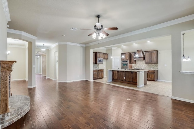 unfurnished living room featuring visible vents, ornamental molding, ceiling fan with notable chandelier, hardwood / wood-style floors, and baseboards