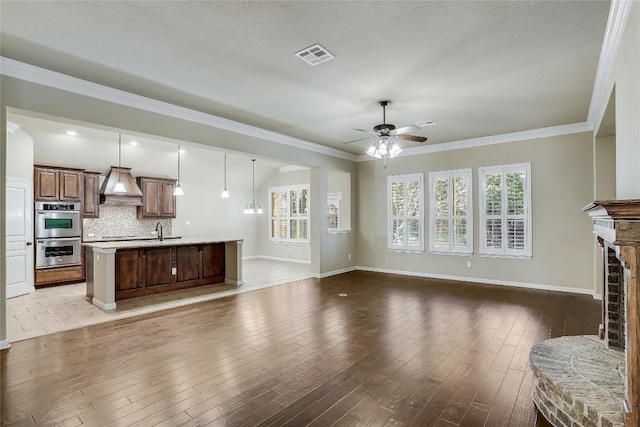 living room with visible vents, a fireplace with raised hearth, ornamental molding, and hardwood / wood-style flooring