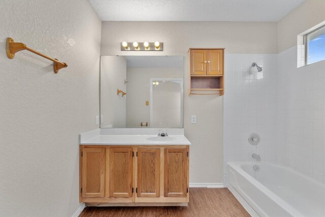 bathroom with wood finished floors, shower / bathing tub combination, baseboards, vanity, and a textured wall