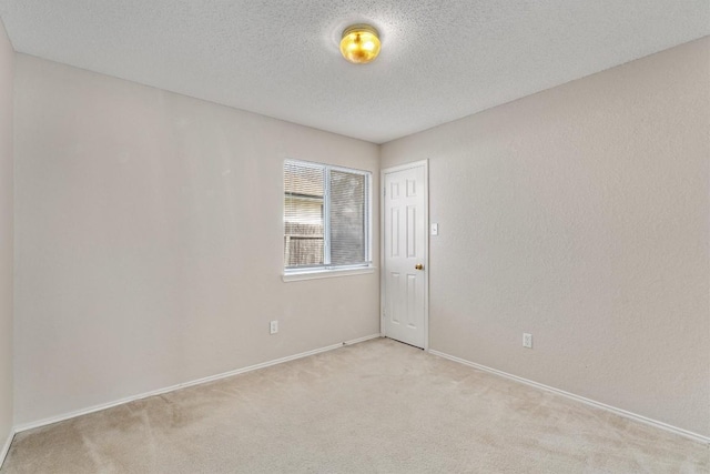 unfurnished room featuring light carpet, a textured ceiling, and baseboards