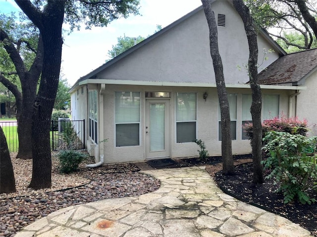 view of front of house featuring fence, roof with shingles, and stucco siding