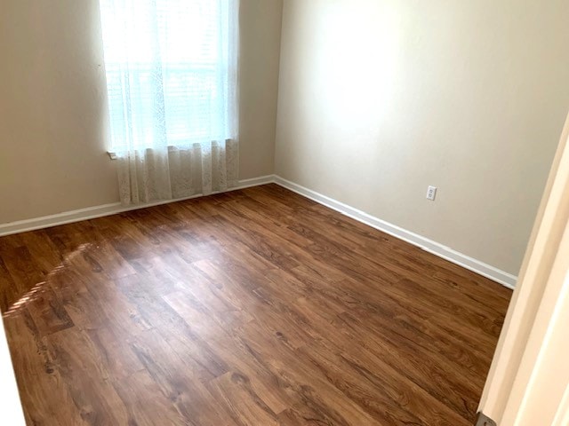 empty room with dark wood-type flooring and baseboards