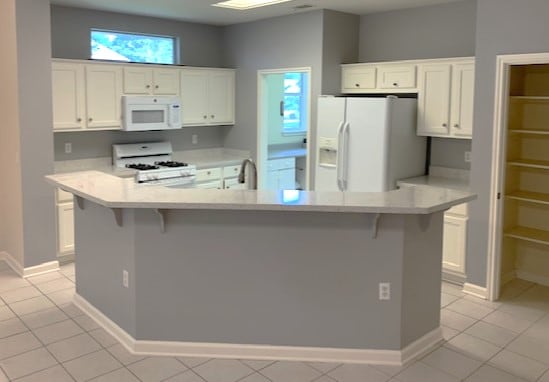 kitchen with a kitchen breakfast bar, white appliances, white cabinets, light tile patterned flooring, and light countertops