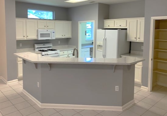 292 Whispering Wind Dr, Georgetown, TX 78633 - kitchen featuring white appliances, white cabinetry, light countertops, a kitchen bar, and light tile patterned floors