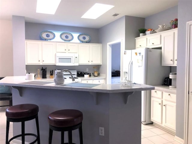 kitchen with white appliances, light tile patterned floors, a skylight, white cabinetry, and a kitchen bar