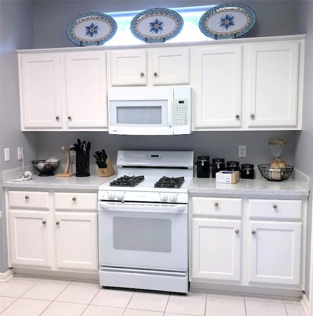 kitchen with light tile patterned floors, white appliances, white cabinets, and light countertops