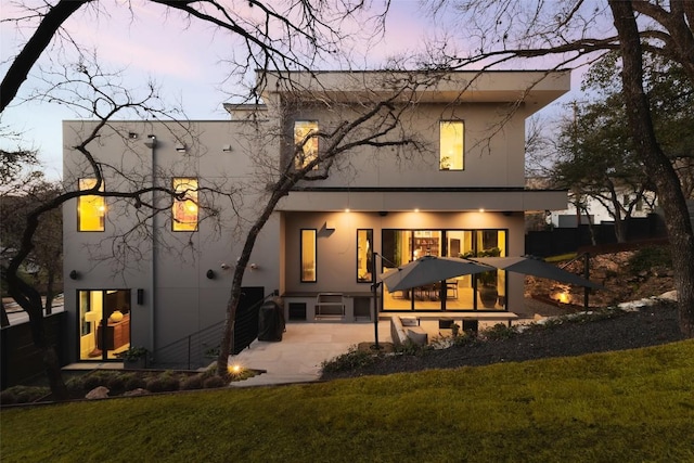 back of property at dusk featuring a yard and stucco siding