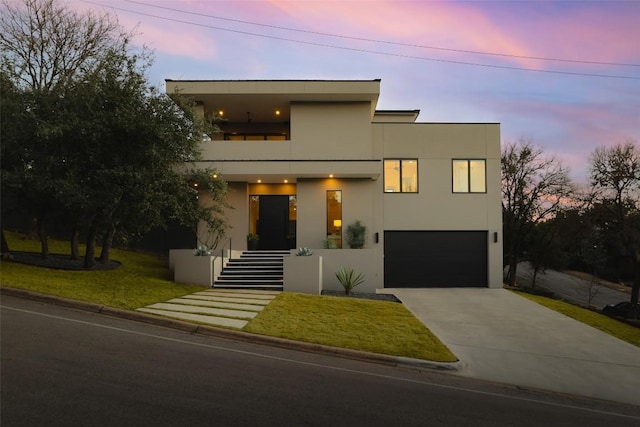 contemporary house with a balcony, driveway, a yard, stucco siding, and a garage