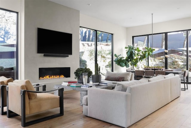 living room featuring a wealth of natural light, light wood-style flooring, and a warm lit fireplace