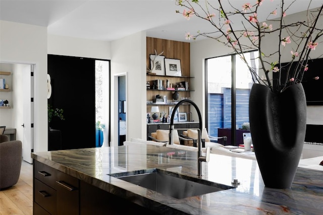 kitchen with dark stone countertops, open floor plan, light wood finished floors, and a sink