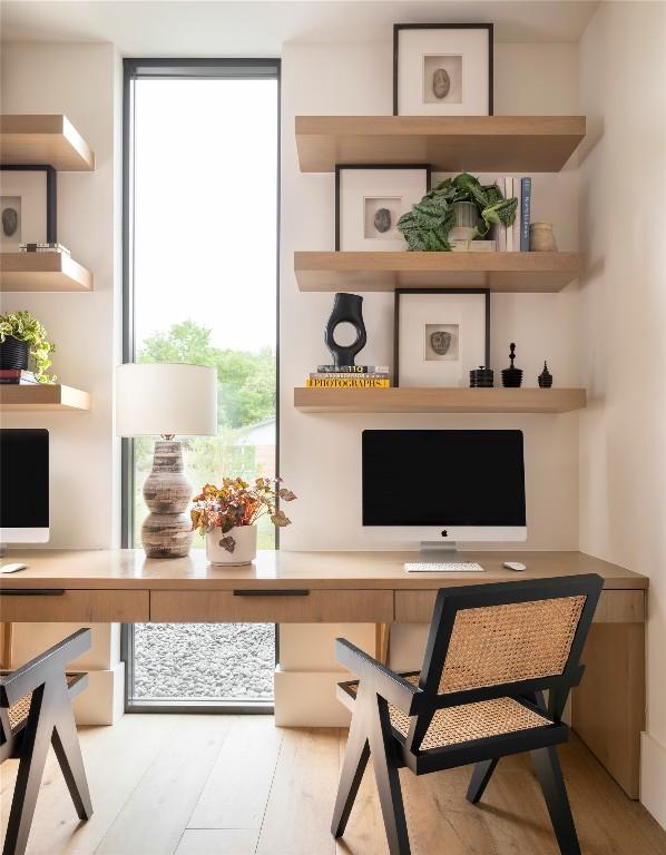 home office with a wall of windows, wood finished floors, and built in desk