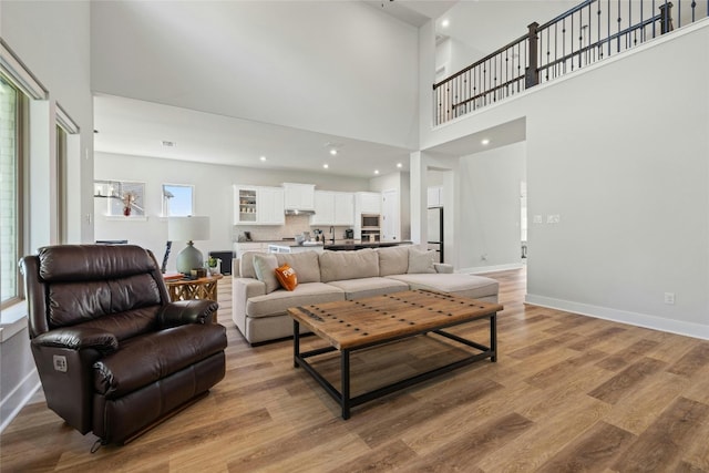 living area with recessed lighting, light wood-type flooring, baseboards, and a towering ceiling