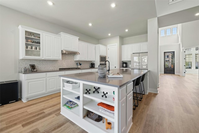 kitchen featuring a large island, under cabinet range hood, a kitchen breakfast bar, tasteful backsplash, and stainless steel appliances