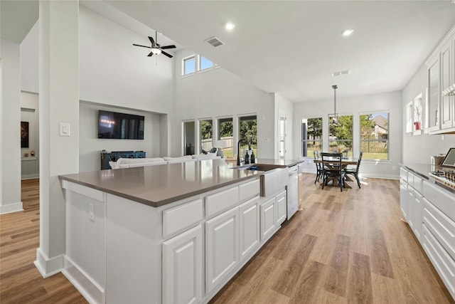 kitchen with white cabinetry, a sink, dishwasher, dark countertops, and light wood-type flooring