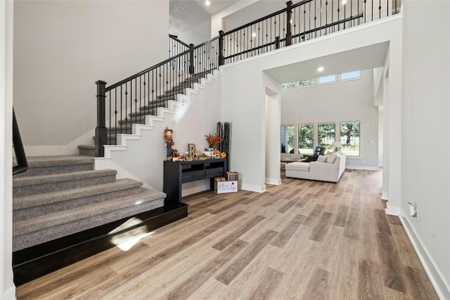 foyer entrance with stairs, wood finished floors, baseboards, and a towering ceiling