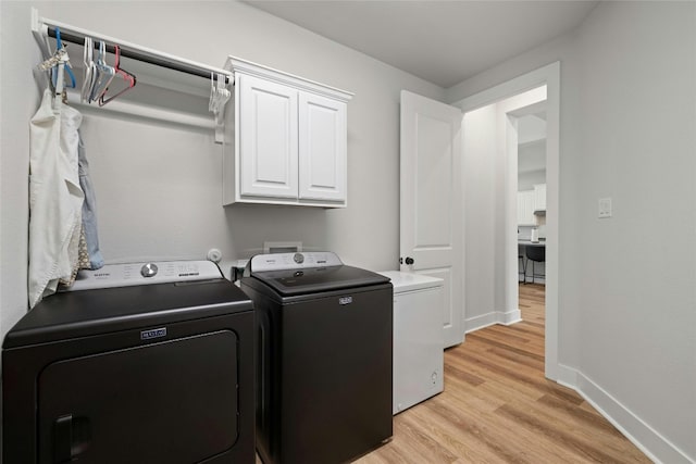 clothes washing area featuring cabinet space, baseboards, light wood finished floors, and washing machine and clothes dryer