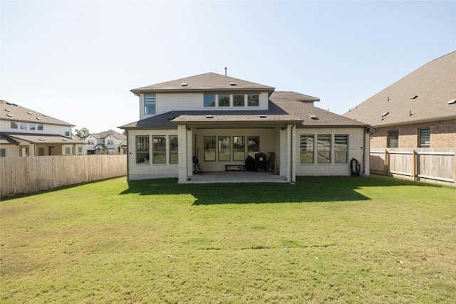 rear view of house with brick siding, a fenced backyard, a shingled roof, a patio area, and a lawn