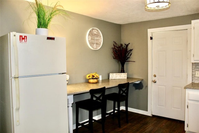 kitchen featuring white cabinetry, dark wood-style floors, baseboards, and freestanding refrigerator