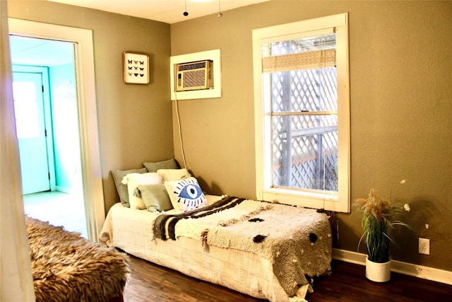 bedroom with an AC wall unit, baseboards, and wood finished floors