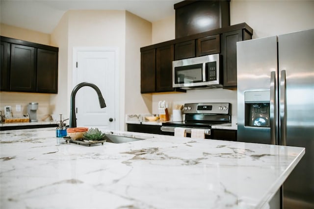 kitchen featuring a sink, light stone countertops, dark brown cabinetry, and appliances with stainless steel finishes