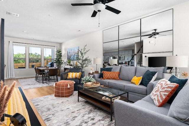 living area featuring visible vents, a ceiling fan, wood finished floors, and stairs