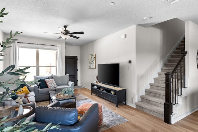 living area featuring stairs, ceiling fan, light wood finished floors, and a textured ceiling