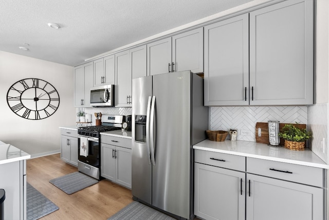 kitchen featuring light wood-style flooring, tasteful backsplash, gray cabinets, and stainless steel appliances