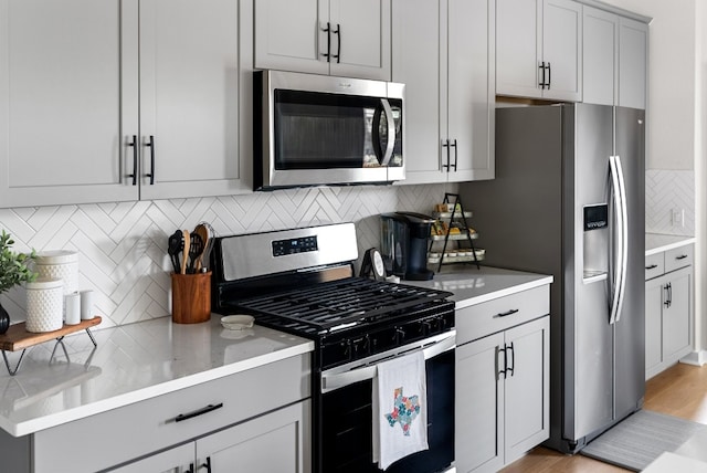 kitchen with decorative backsplash, gray cabinetry, light wood-type flooring, and stainless steel appliances