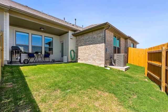 rear view of house with brick siding, central AC unit, a yard, and fence