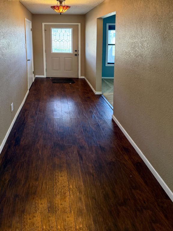 doorway to outside featuring a textured wall, baseboards, a textured ceiling, and hardwood / wood-style flooring