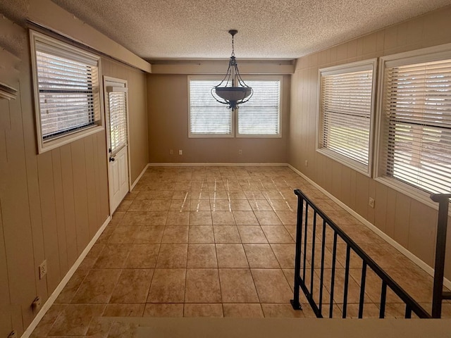 unfurnished dining area featuring tile patterned floors, baseboards, wood walls, and a textured ceiling