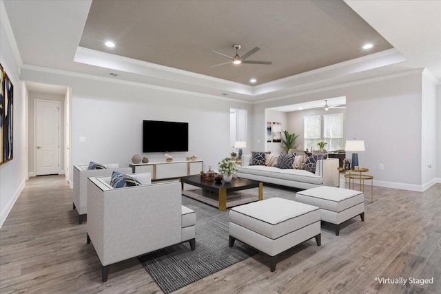 living area with crown molding, baseboards, ceiling fan, light wood-style flooring, and a raised ceiling