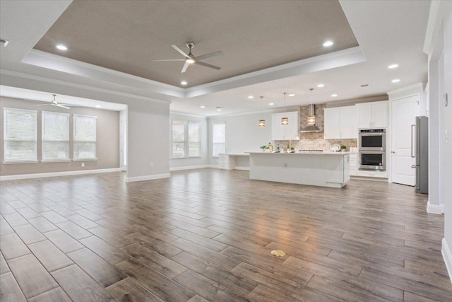 unfurnished living room with ceiling fan, dark wood-type flooring, crown molding, and a tray ceiling