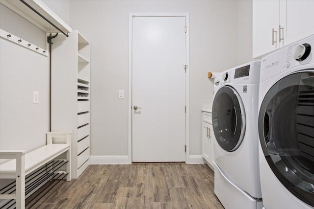 clothes washing area featuring baseboards, cabinet space, wood finished floors, and washing machine and clothes dryer